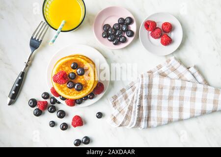 Dolci frittelle fatte in casa con mirtilli e lamponi. Gustosa colazione con succo di frutta. Vista dall'alto. Foto Stock