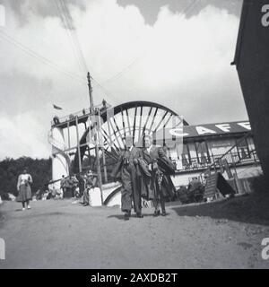 Anni '1930, storica, coppia fuori dal caffè della Laxey Wheel sull'Isola di Man, una ruota idraulica vittoriana costruita per pompare l'acqua dalle miniere di Laxey. Conosciuta anche come Lady Isbella, è la più grande ruota idraulica funzionante del mondo. Foto Stock