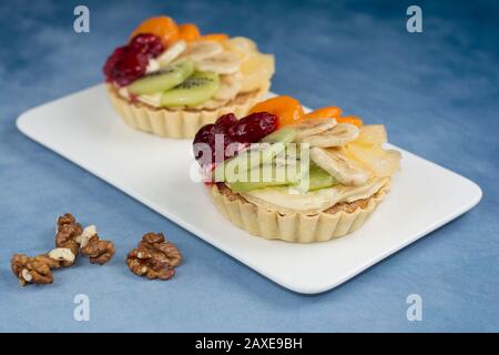 Ciotole di pasta commestibili con ripieno di noci e crema, fette di kiwi e banana, pezzi di ananas e frutti di lampone, su una piastra bianca Foto Stock