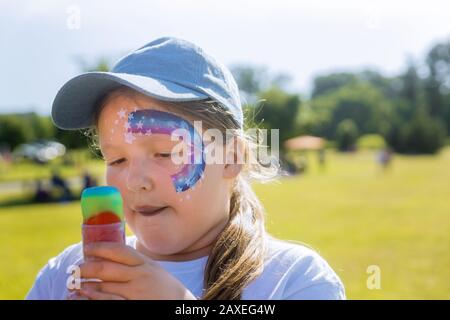 Teenager con la vernice del viso che mangia il gelato di colore della ciotola della pioggia. Foto Stock