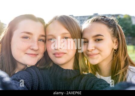 Tre ragazze adolescenti di 12-14 anni, città estiva guardare video telefono, felice sorridente persone divertirsi gioire. Selfie ritratto primo piano. Casual Foto Stock