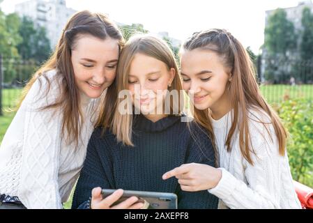 Tre ragazze adolescenti di 12-14 anni, città estiva guardare video telefono, felice sorridente persone divertirsi gioire. Reti sociali Internet Foto Stock