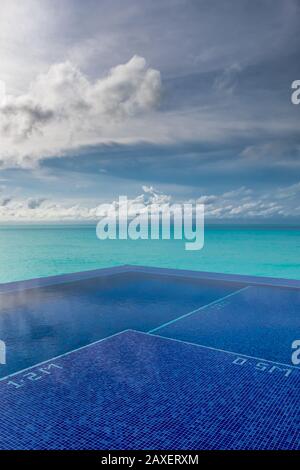 Una piscina a sfioro blu brillante accanto al mare turchese con nuvole tempestose su un'isola delle Maldive Foto Stock