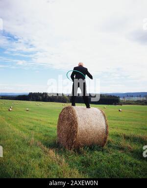 Vista posteriore di un uomo in piedi su una balla di fieno che gioca con un cerchio di plastica, Germania Foto Stock