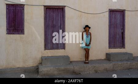Asian Woman in occhiali da sole e cappello in piedi di fronte alla casa tradizionale greca con persiane e porte viola nel villaggio di Eressos sulle isole di Lesv Foto Stock