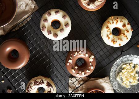 Colpo verticale di deliziose ciambelle coperte di bianco e. glassa di cioccolato marrone su un tavolo nero Foto Stock