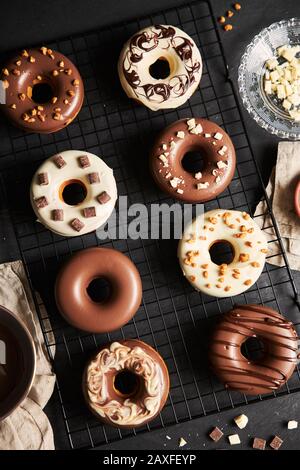 Colpo verticale di deliziose ciambelle ricoperte di glassa al cioccolato con gli ingredienti su un tavolo Foto Stock