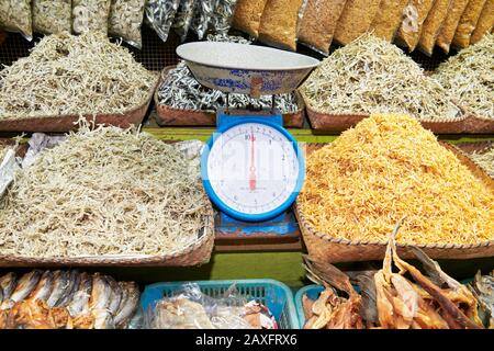 Primo piano di cumuli di piccoli pesci secchi e salati in cestini di bambù, accanto ad una bilancia di pesatura analogica, in un mercato di Iloilo, Filippine, Asia Foto Stock