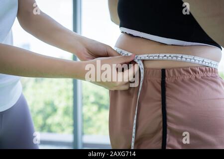 Giovane allenatore femminile che misura lo strato di grasso di donna in sovrappeso con cintura in forma fisica Foto Stock
