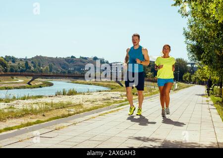 Colpo di giovane donna e uomo che corre attraverso il riverside via Foto Stock