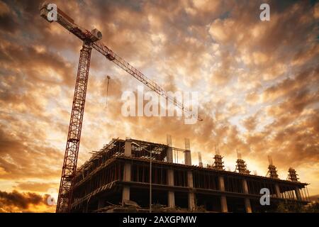 Silhouette di un edificio con una gru da cantiere contro il tramonto e le nuvole. Edifici e concetto di costruzione Foto Stock