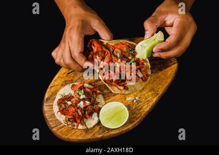 Tacos al pastore piatto si adagia su uno sfondo nero, con una persona che stringe calce su di esso. Autentici tacos messicani con carne marinata, cipolla, ananas Foto Stock