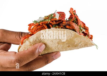 Primo piano di una mano che tiene autentico taco al pastore messicano su uno sfondo bianco Foto Stock