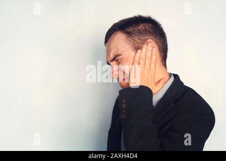 L'uomo con le orecchie sta tenendo il suo concetto dolorante del dolore dell'orecchio del corpo. Un uomo d'affari o lavorare con tinnito. Copia spazio Foto Stock