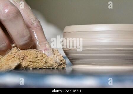 Il vasaio rende il vaso di terra vicino. Mani macchiate nella creta e la piastra di creta Foto Stock