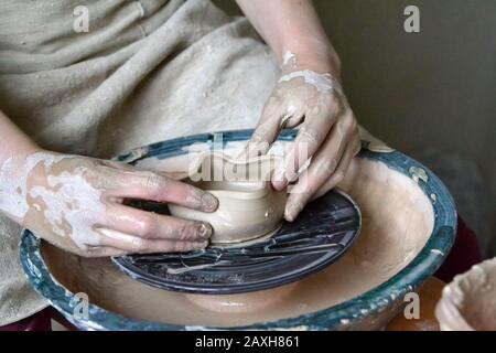 persona vasaio fa terra di creta pentola su una ruota del vasaio in laboratorio di ceramica Foto Stock