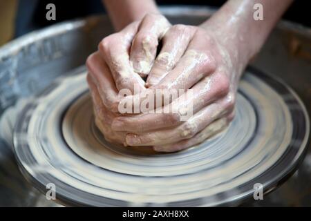 Il vasaio principale piegato insieme le mani scolpisce un prodotto di creta su una rotella del vasaio. Pelle della mano macchiata con argilla e bagnata Foto Stock