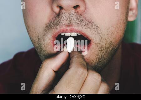 pillole maschili. faccia da vicino. pillola in bocca. l'uomo cigni una pillola di dolore bianco. Ragazzo beve medicina. Paziente Foto Stock