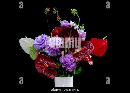 Bouquet di fiori colorati con fiori di Flamingo rosso e bianco, Lisanthus viola o Eustoma e arrotolato felce isolato su sfondo nero Foto Stock