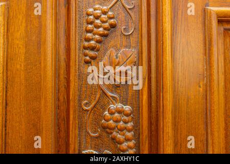 Grappoli e foglie di uva sono scolpiti sulla porta di legno anteriore del cottage e coperti con vernice. Porta anteriore in rovere Foto Stock