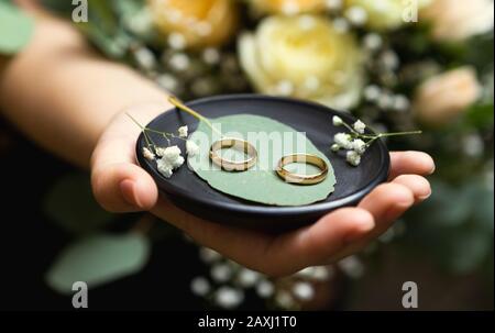 Coppia di anelli di nozze d'oro su foglie verdi nel palmo della donna Foto Stock