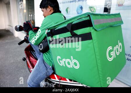 Antipolo City, Filippine - 11 febbraio 2020: Il pilota del servizio di consegna di cibo popolare del motociclo naviga il suo smartphone e aspetta un ordine. Foto Stock