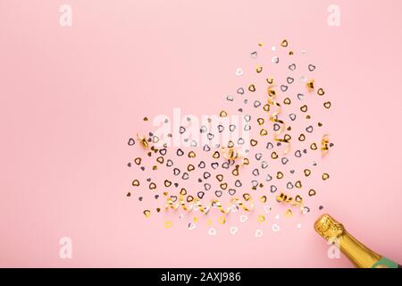 Bottiglia di champagne con confetti dorati cuori su rosa Foto Stock