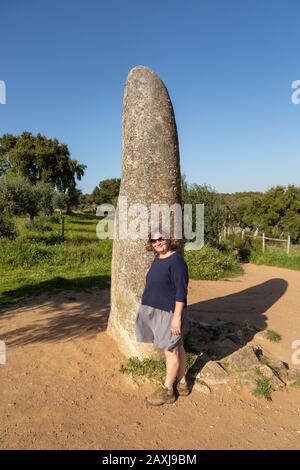 Donna di media età in piedi dalla pietra neolitica alta 4 metri chiamato il Menir dos Almendres, vicino Evora, Alentejo, Portogallo Foto Stock