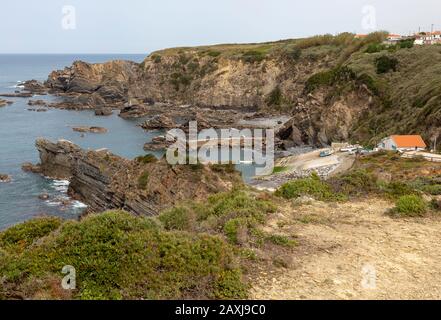 Costa rocciosa e frastagliata vicino al villaggio portuale di pescatori di Azenha do Mar, Alentejo Littoral, Portogallo, Europa meridionale, piccola barca da pesca in arrivo Foto Stock