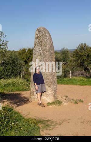 Donna di mezza età in piedi dalla pietra neolitica alta 4 metri chiamato il Menir dos Almendres, vicino Evora, Alentejo, Portogallo, Foto Stock