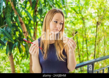 Donna tiene eco naturale spazzolino di bambù e in altri denti di plastica mano. Sfondo rustico. Concetto di stile di vita sostenibile. Zero rifiuti. Scelta Foto Stock