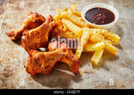 Gustoso spuntino con ali di pollo alla griglia speziate servite con patatine crocchette tagliate a pezzetti e un piatto laterale di peperoncino in un vecchio vassoio di cottura in metallo vintage Foto Stock