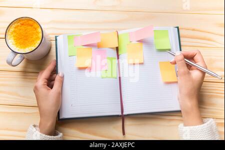 Donna giorno di pianificazione con adesivi colorati e tazza di latte caldo con curcuma Foto Stock