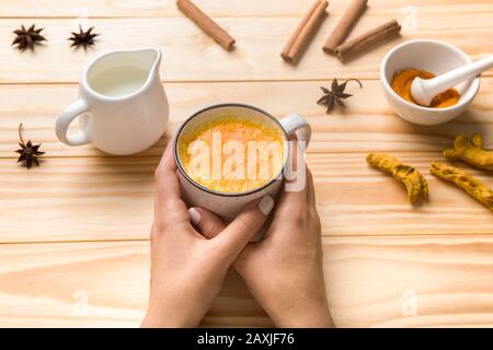 Mani femminili che tengono una tazza di latte con spezie, miele e polvere di curcumino Foto Stock