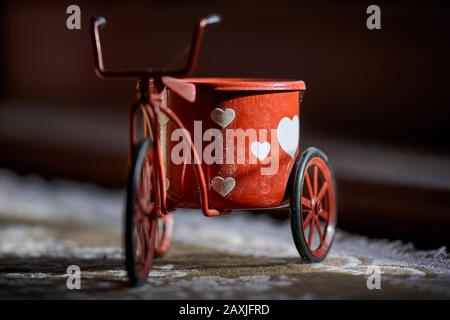 Primo piano di un piccolo triciclo antico con un piccolo vaso di fiori e cuori in piedi su un tappeto illuminato dal sole Foto Stock