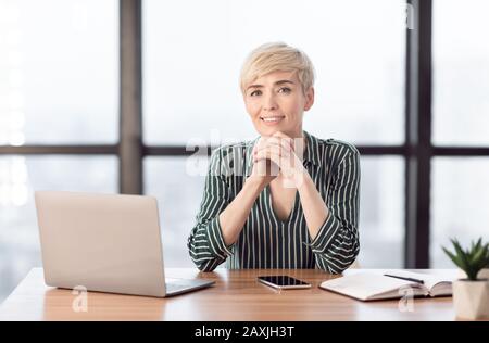 Confident Business Lady Al Laptop Che Posa Seduto In Ufficio Moderno Foto Stock