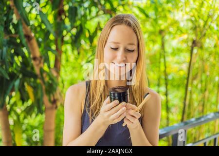 Giovane donna spazzolare i denti usando polvere di carbone Attivo per spazzolare e sbiancare i denti. Spazzola ecologica di bambù Foto Stock