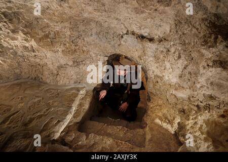 Un turista che visita una grotta all'interno del Sacro Monastero Greco Ortodosso di Sarantarion montagna o Tentazione costruita sulle pendici del Monte Delle Tentazioni situato lungo una scogliera che domina la città di Gerico nei territori Palestinesi situati vicino al fiume Giordano nella Cisgiordania, Israele Foto Stock