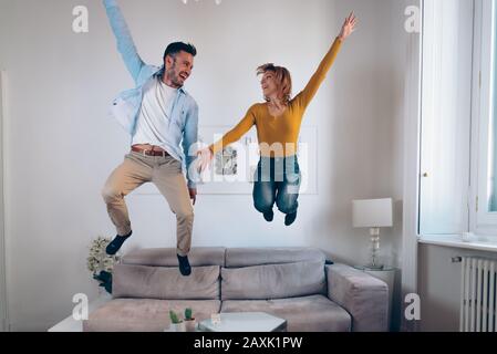 Felice coppia innamorata divertirsi insieme saltando sul divano nel soggiorno a casa. Concetto di attività per il tempo libero Foto Stock