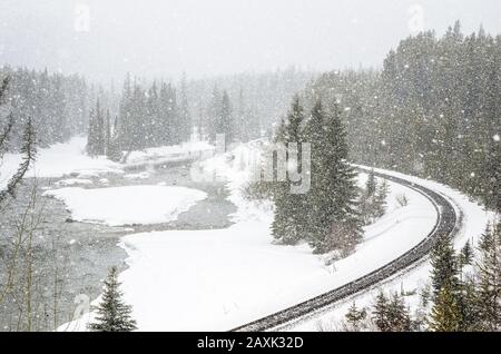 Linea ferroviaria che corre lungo un fiume di montagna durante una Blizzard Foto Stock