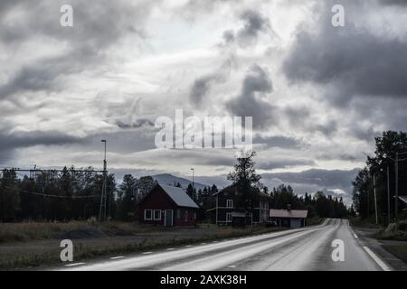 Spettacolare percorso scandinavo settentrionale con case tradizionali rosse svedesi. Superstrada fredda per il Nord europa. Natura foresta, montagne vista prospettiva strada Foto Stock