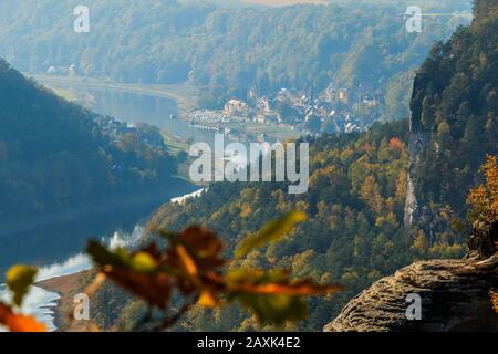 Vista sulla valle dell'Elba nella Svizzera sassone. Corso sul fiume con sole e alberi in autunno. Rocce ed edifici in luce naturale sul Monte Elbsandstein Foto Stock