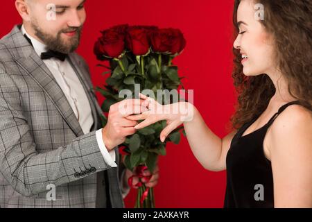 Vista ritagliata dell'uomo che mette l'anello sul dito girlfriends isolato su sfondo rosso. Foto Stock