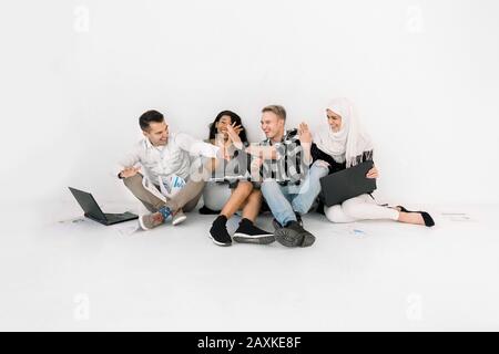Studio girato di quattro bei giovani amici multiculturali. Divertente gente sorridente allegramente ed avere divertimento mentre dà cinque a vicenda dopo il duro lavoro Foto Stock