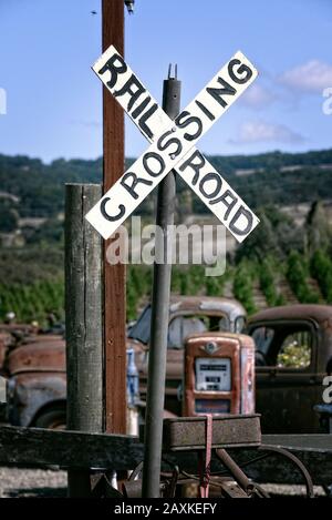 Segno di attraversamento della ferrovia e vecchie auto arrugginite con pompe a gas in una fattoria nella contea di Sonoma, California, Stati Uniti Foto Stock