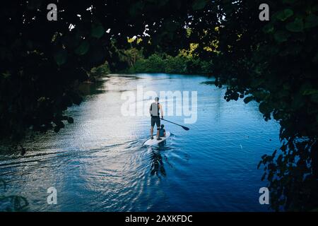 Vista ad alto angolo dell'uomo e del suo figlio pagaia imbarco lungo un fiume giungla. Foto Stock