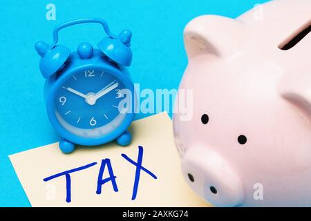 Banca piggy, sveglia e foglio di carta su sfondo blu. Concetto sul tema: Tempo di raccogliere soldi per le tasse Foto Stock