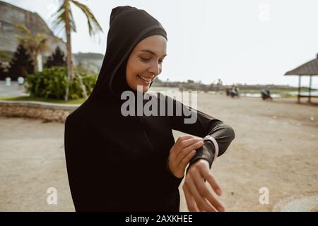 giovane donna musulmana con sciarpa impostazione smart watch prima di jogging Foto Stock