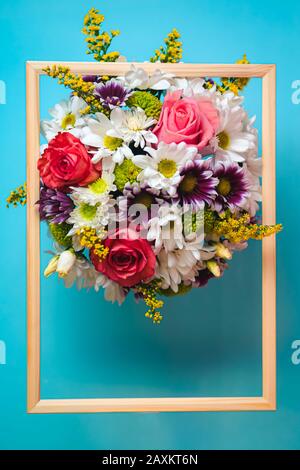 Bouquet di rose e margherite su sfondo azzurro e rosa con cornice in legno e spazio per il testo. Vista dall'alto. Concetto di evento. Foto Stock