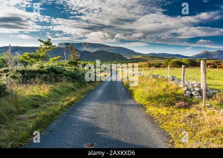 Strada di campagna attraverso il paese di Ballyboe verso Muckish Mountain (An Mhucais), parte della catena montuosa di Derryveagh, County Donegal, Irlanda Foto Stock